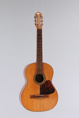 an acoustic guitar hanging from a string on a white wall