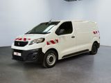 La camionnette blanche est garée dans une grande pièce ; elle porte une bande rouge sur le côté.