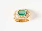 gros plan d'une bague en or avec une pierre verte et des diamants