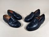 three pairs of black loafers are lined up on a white surface