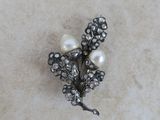 une broche ancienne en argent, ornée de perles et de fleurs, posée sur une surface en marbre