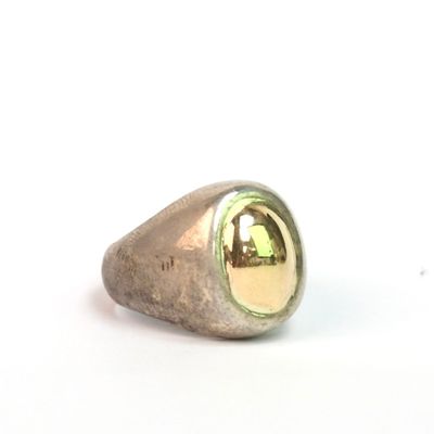 bague en argent et en or sur fond blanc, avec le reflet d'un immeuble