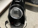 a black coffee maker sitting on the floor next to a trash can