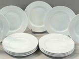 twelve white dinner plates stacked on top of each other on a table