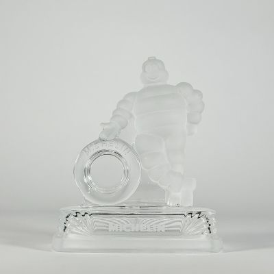 figurine en verre transparent représentant un homme tenant une bague, posée sur un socle