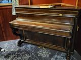 un piano dans un coin d'une pièce où sont accrochés des tableaux au mur
