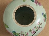 a green vase with flowers painted on it on a table