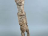 une vieille statue en bois représentant un homme, posée sur un socle noir