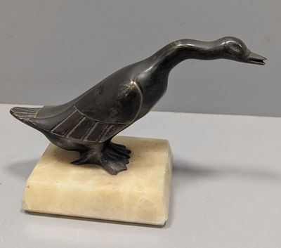 statue d'un canard posée sur un socle en marbre, sur une surface blanche
