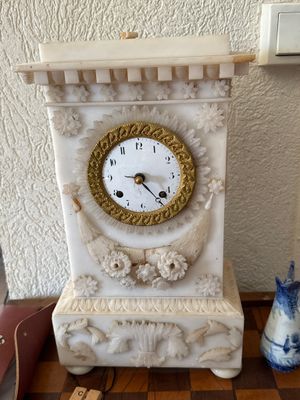 a white clock sitting on top of a table next to a blue vase