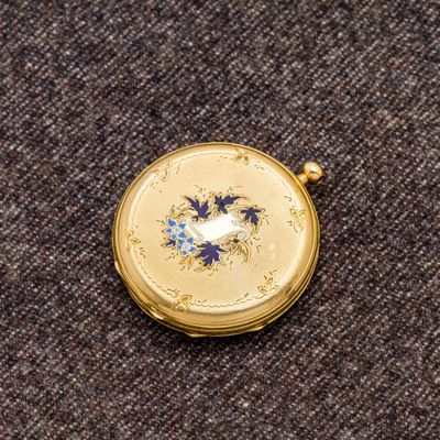 une petite montre de poche en or ornée de fleurs bleues