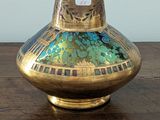 a gold vase sitting on a wooden table with a white wall in the background