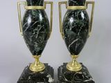 paire de vases noirs et dorés munis d'anses, posés sur des socles en marbre