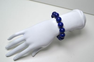 une main de mannequin blanche tenant un bracelet bleu en perles