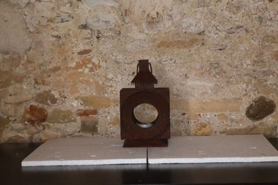 une petite horloge posée sur une table devant un mur de pierre