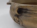 a large bronze bowl with a handle on a white surface