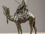 bronze statue of a man riding a camel with a stick in his hand