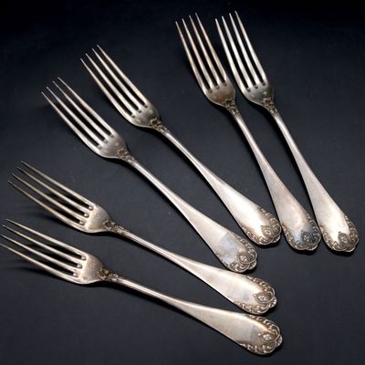 six silver forks with ornate designs on them on a black surface