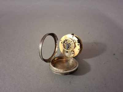 a silver pocket watch sitting on a table next to a ring
