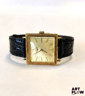 une montre en or avec un bracelet en cuir noir posée sur une surface blanche