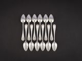 six cuillères en argent sont disposées en rangée sur une surface noire