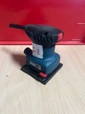 un gros plan d'une ponceuse posée sur une table, sur fond rouge
