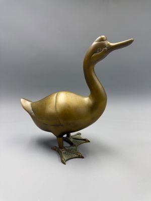 a brass duck figurine sitting on a white surface