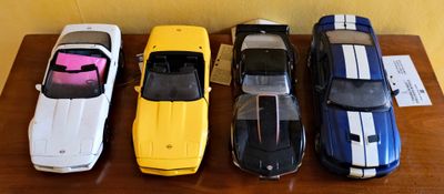 Plusieurs petites voitures sont alignées sur une table devant un mur jaune.