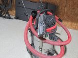 un aspirateur posé par terre, muni d'un tuyau rouge