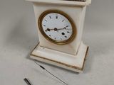 a small white clock with a gold rim and a key