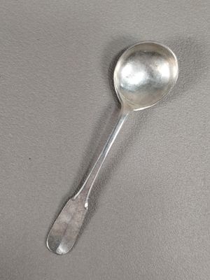 une cuillère en argent posée sur une surface grise, avec une cuillère au milieu de celle-ci