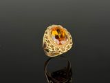 a gold ring with an oval citrine stone surrounded by a filigree band