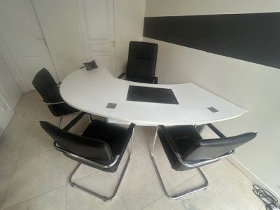 Un large bureau à plateau cintré en stratifié blanc. On y jo…