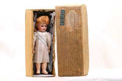 une petite poupée dans une boîte en carton posée sur une surface blanche