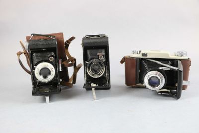 two old fashioned cameras sitting side by side on a white surface