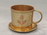 une tasse et une soucoupe en or ornées d'une ancre