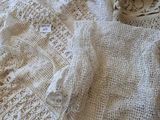 un pull blanc au crochet posé sur un lit, à côté d'une paire de chaussures