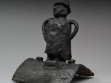 statue représentant un homme debout sur un morceau de bois, coiffé d'un chapeau