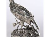 un oiseau en métal argenté posé sur un rocher, sur fond blanc