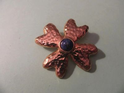 un gros plan d'une broche en forme de fleur ornée d'une pierre bleue au centre