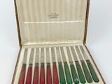 six knives in a wooden case with red and green handles