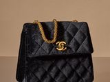 a close up of a black purse on a table with a gold chain