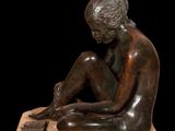 bronze statue of a woman sitting on a wooden base