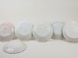 six white and pink plates and a white plate on a white surface