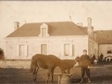 une vieille photo représentant un homme et un cheval devant une maison