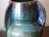 a blue vase sitting on a table with a white wall in the background
