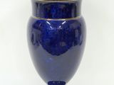 un vase bleu bordé d'or posé sur une surface blanche