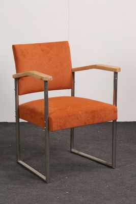 une chaise orange posée sur un sol noir, près d'un mur blanc