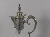 a silver and glass pitcher with a handle on a table
