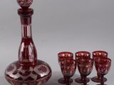 une carafe en verre rouge, avec six verres à vin à côté